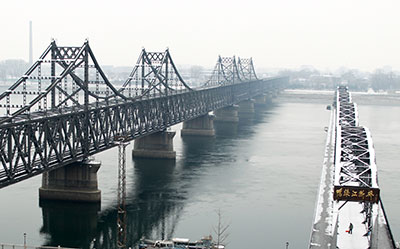 A man shovels snow on the destroyed Yalu bridge, right, next to the Friendship Bridge linking China and North Korea. (AP/Aritz Parra)