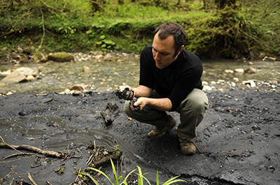 Сурен Газарян исследует чёрное вещество найденное в глине недалеко от Сочи. (AFP/Mikhail Mordasov)