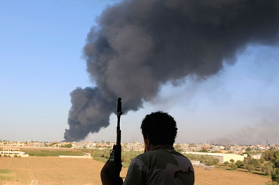 A fighter watches as smoke rises after rockets fired by one of Libya's militias struck a fuel tank in Tripoli on August 2. (Reuters/Hani Amara)