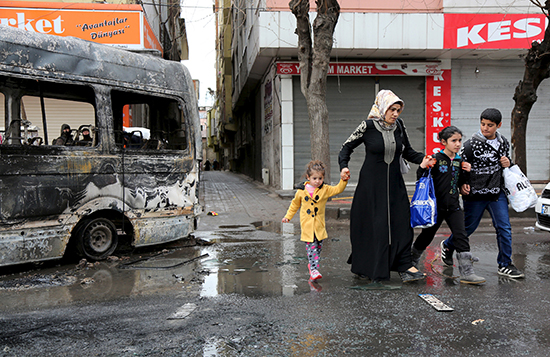 A woman and children walk past a bus damaged in fighting between ethnic Kurdish youth and security forces, in the southeastern Turkish city of Diyarbakir, March 15, 2016. Pro-Kurdish journalists have faced terrorism charges for their reporting on clashes between ethnic Kurdish youth and security forces in the region since peace talks between the Kurdistan Workers' Party (PKK) and the government unraveled in 2015. (Sertac Kayar/Reuters)