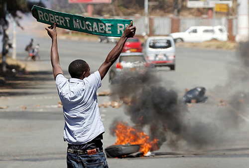 A man carries a street sign in Harare as protesters clash with police on August 26. Journalists have been beaten and detained while covering unrest in Zimbabwe. (Reuters/Philimon Bulawayo)