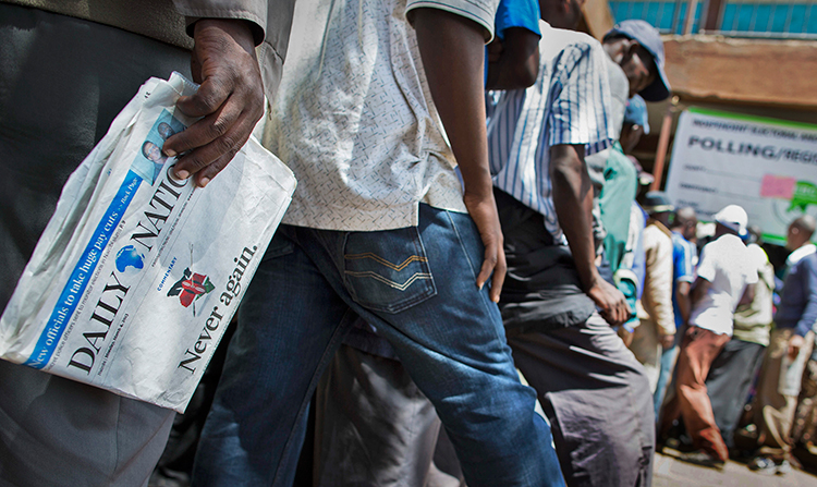 A Kenyan voter in Nairobi carries a copy of the Daily Nation newspaper as he waits to vote in the March 4, 2013, elections. The headline, "Never Again," refers to the post-election violence of 2007. (AP/Mackenzie Knowles-Coursin)