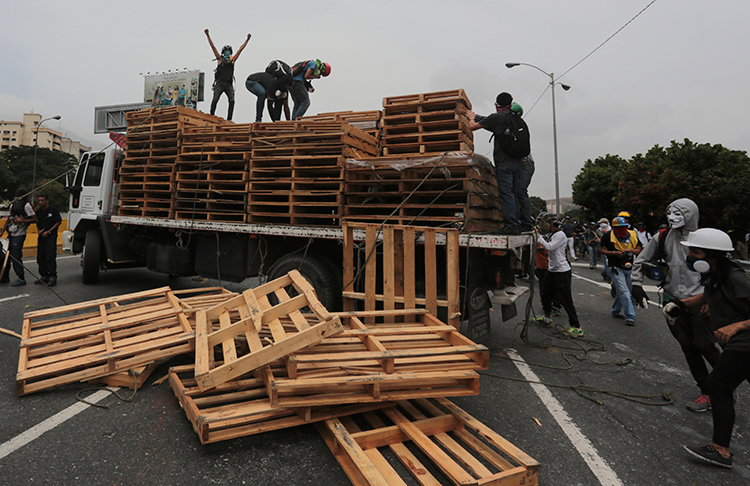 Manifestantes descargan tarimas de madera de un camión al que obligaron a parar en una autopista en Caracas, el 22 de mayo de 2017. (AP/Fernando Llano)