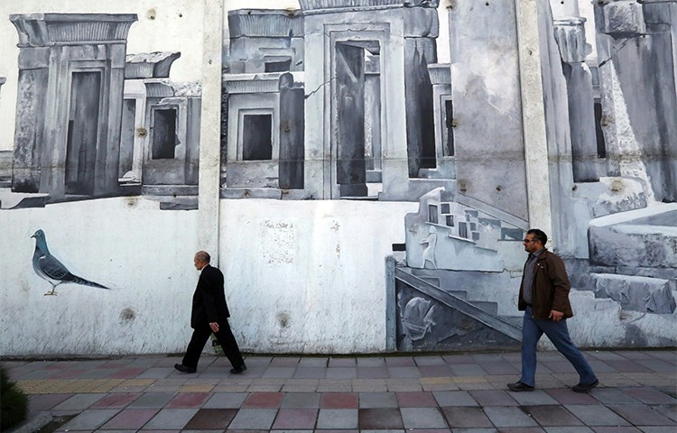 Iranians walk past street art in the southwestern district of Tehran in January 2016. Security agents arrested two journalists in the city in August (AFP/Atta Kenare)