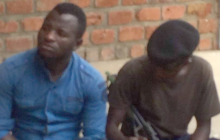 DRC journalist Benjamin Mutiya, left, pictured under police guard on December 18, is detained on defamation accusations. (Fortunat Maronga/CJDH)