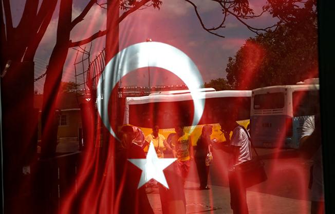 People reflected on glass with Turkish a flag at a bus station in Istanbul in July 2016. A proposed bill presented to Turkey's parliament on February 2 would force online broadcasters, including YouTube and Netflix Turkey, to be licensed and regulated by the federal TV and radio watchdog group RTÜK, according to local reports. (AP/Petros Karadjias)