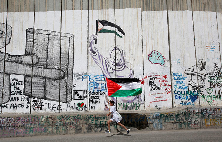 A Participant runs past the Israeli barrier during the annual Palestine Marathon in Bethlehem, in the occupied West Bank, March 23, 2018. Israeli troops on March 23 detained Bakr Abdel Haq, a correspondent for the Palestinian Authority's broadcaster Palestine TV, at the al-Karama border crossing between Israel and Jordan.(Reuters/Mussa Qawasma)