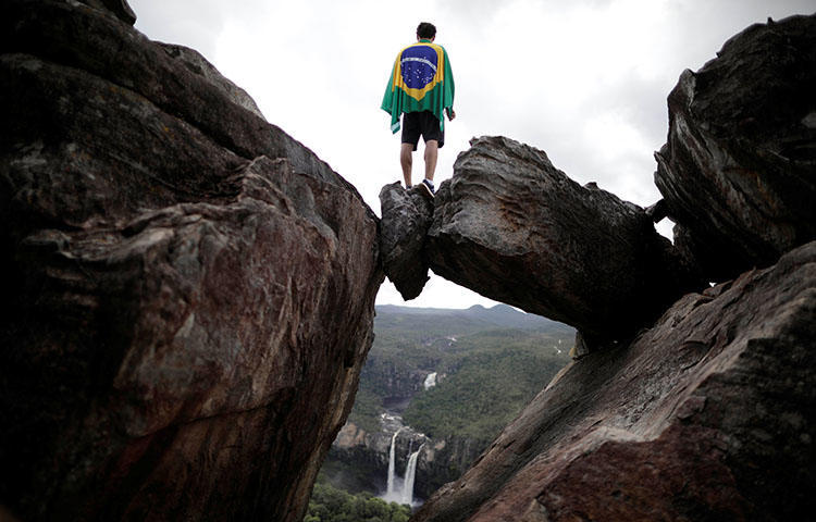 Un visitante al parque envuelto en una bandera brasileña se para sobre una ventana natural de piedras en el Parque Nacional Chapada dos Veadeiros en Alto Paraíso, Brasil en marzo de 2018. Al menos un sujeto armado no identificado disparó contra las oficinas del semanario Jornal dos Bairros el 25 de marzo, según informes. (Reuters / Ueslei Marcelino)