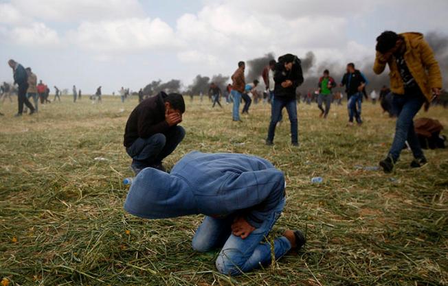 Palestinian protesters cover from teargas fired by Israeli soldiers during clashes with Israeli troops along the Gaza Strip border with Israel, east of Khan Younis, Gaza Strip, on March 30, 2018. (AP/Adel Hana)