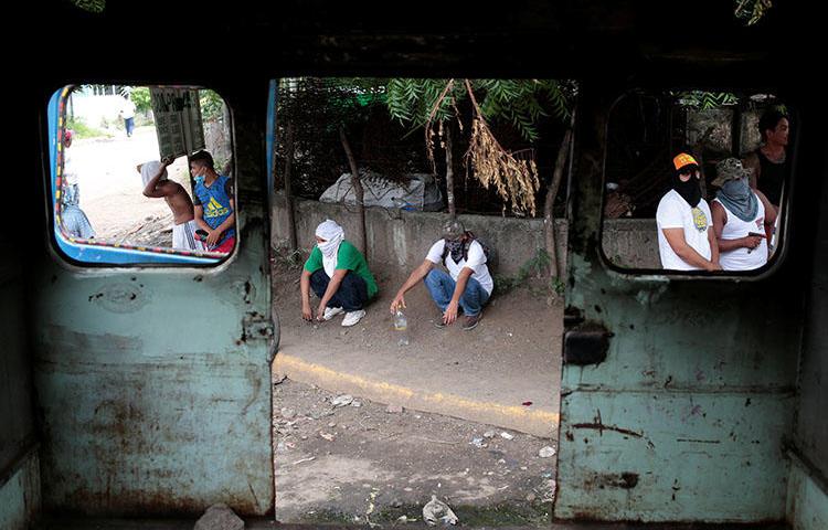 Protesters stand behind a burned bus during an anti-government rally in Tipitapa, Nicaragua on June 14. A Nicaraguan reporter who is covering the unrest says armed attackers broke into his home, beat him, and stole his identification documents. (Reuters/Oswaldo Rivas)