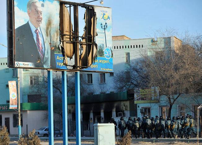 Kazakh Interior Ministry troops patrol beneath a poster of President Nursultan Nazarbayev and partially burnt buildings in Zhanaozen, in December 2011, that were damaged in riots. Kazakh police detained a French journalists today while he interviewed witnesses to the 2011 violence. (Reuters/Vladimir Tretyakov)