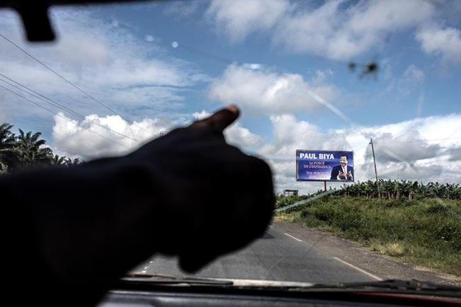 A taxi driver points towards an electoral poster for Cameroonian President Paul Biya as the road crosses into the majority English-speaking South West region of Cameroon, in Buea, on October 3, 2018. A journalist was detained October 23 after publishing articles criticizing the government's handling of grievances of Anglophone Cameroonians. (AFP/Marco Longari)