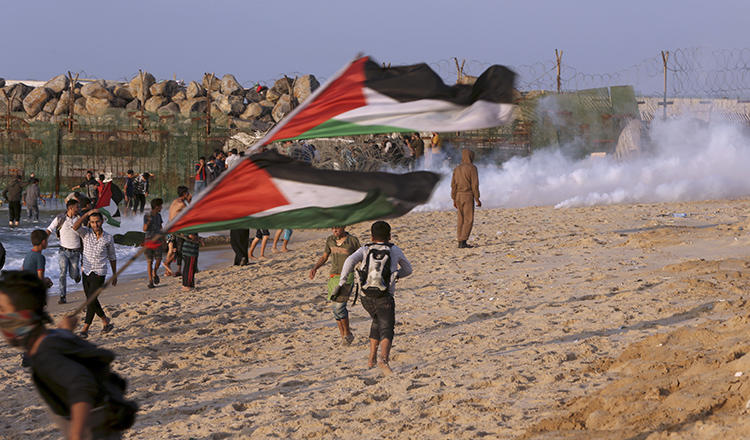 Protesters take cover from teargas fired by Israeli troops near the fence of the Gaza Strip border with Israel during a protest on the beach near Beit Lahiya, northern Gaza Strip, on November 19, 2018. (AP Photo/Adel Hana)