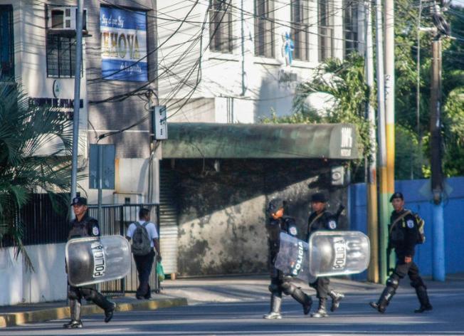 Policiais do choque caminham em frente à estação noticiosa a cabo e internet 100% Noticias, em Manágua, em 22 de dezembro de 2018, um dia depois de a emissora ter sido invadida e fechada pela polícia nicaraguense. Dois jornalistas foram presos durante a incursão. (AFP / Maynor Valenzuela)