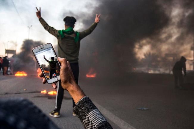 A protester uses his cell phone to film at a demonstration in Basra in January. Militias and Iraqi security forces are attacking and detaining journalists who cover protests in the city. (AFP/Hussein Faleh)