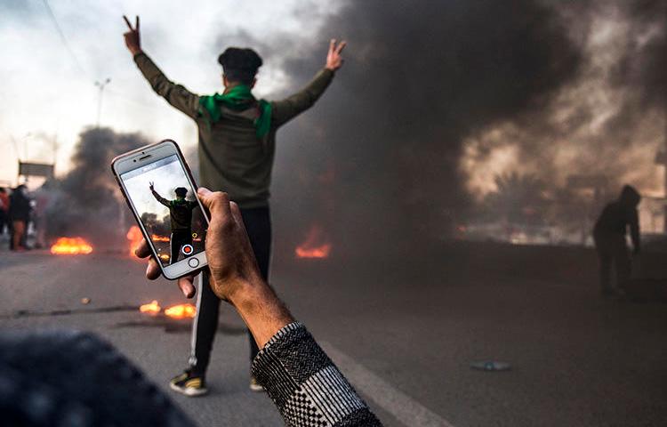 A protester uses his cell phone to film at a demonstration in Basra in January. Militias and Iraqi security forces are attacking and detaining journalists who cover protests in the city. (AFP/Hussein Faleh)