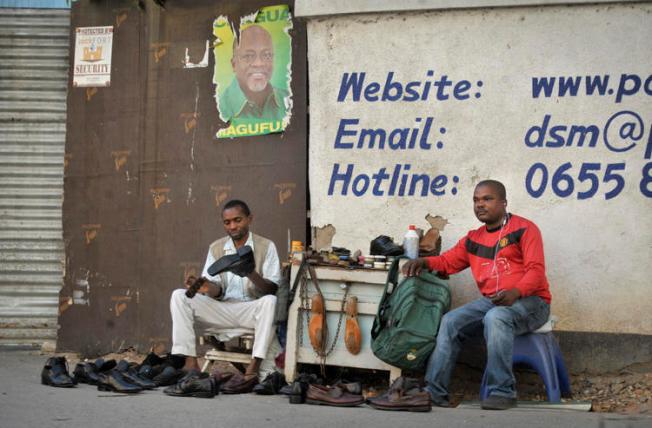 A Tanzanian shoe-shiner conducts his business underneath an election poster for then ruling party presidential candidate, and later president, John Magufuli, in Dar es Salaam, Tanzania, on October 27, 2015. On March 28, 2019, the East African Court of Justice found that multiple sections of Tanzania's Media Services Act restrict press freedom. (AP Photo/Khalfan Said)