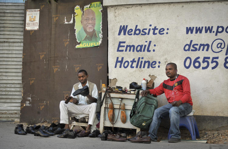 A Tanzanian shoe-shiner conducts his business underneath an election poster for then ruling party presidential candidate, and later president, John Magufuli, in Dar es Salaam, Tanzania, on October 27, 2015. On March 28, 2019, the East African Court of Justice found that multiple sections of Tanzania's Media Services Act restrict press freedom. (AP Photo/Khalfan Said)