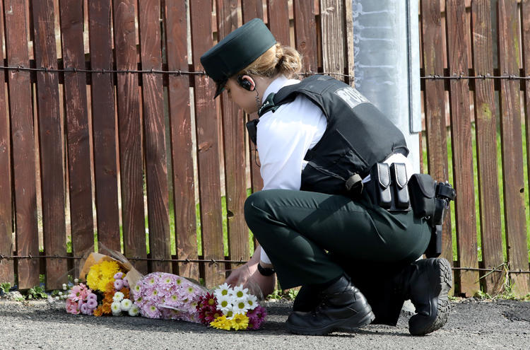 A police officer lays flowers passed to her by members of the public at the scene where journalist Lyra McKee was fatally shot amid rioting overnight in the Creggan area of Londonderry in Northern Ireland on April 19, 2019. (AFP/Paul Faith)