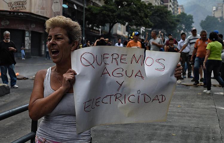 Una mujer sostiene una pancarta que dice 'Queremos Agua y Electricidad' durante una protesta durante el corte de electricidad en Venezuela, en la Avenida Fuerzas Armadas en Caracas el 31 de marzo de 2019. La policía venezolana detuvo al reportero Danilo Gil mientras cubría protestas el 30 de marzo en Ciudad Ojeda, y lo imputaron por resistencia a la autoridad. (AFP/Federico Parra)