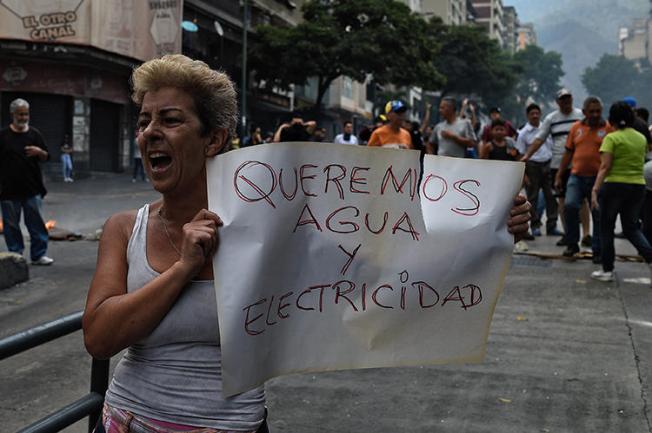 Una mujer sostiene una pancarta que dice 'Queremos Agua y Electricidad' durante una protesta durante el corte de electricidad en Venezuela, en la Avenida Fuerzas Armadas en Caracas el 31 de marzo de 2019. La policía venezolana detuvo al reportero Danilo Gil mientras cubría protestas el 30 de marzo en Ciudad Ojeda, y lo imputaron por resistencia a la autoridad. (AFP/Federico Parra)