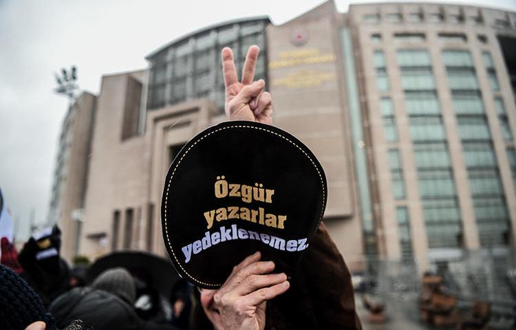 A man holds a sign reading 'Writers' freedom is not guaranteed' outside an Istanbul court during a trial connected to the now shuttered paper Özgür Gündem, in December 2016. A court sentenced seven former journalists from the paper to prison on May 21, 2019. (AFP/Ozan Kose)