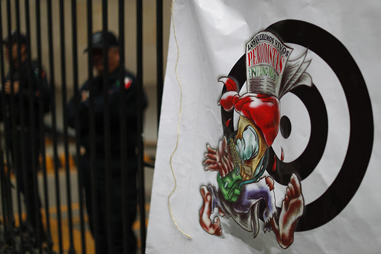 A banner featuring a cartoon of an injured journalist and a headline in Spanish reading, 'We want journalists alive. Not one more,' hangs outside the Secretary of the Interior building in Mexico City on August 21. A reporter was stabbed to death in the state of Estado de México on August 24. (AP/Rebecca Blackwell)