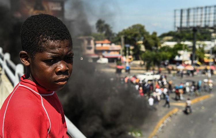 Un garçon regarde les manifestants qui demandent la démission du Président Jovenel Moïse à Port-au-Prince le 4 octobre. Un journaliste radio qui avait été critique à l’égard des troubles et avait été menacé à cause de ses reportages, a été tué à Mirebalais en octobre. (AFP/Chandan Khanna)
