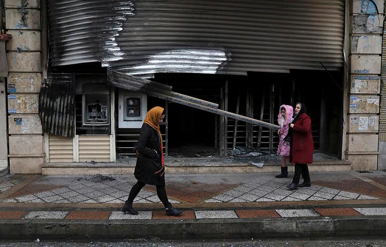 People walk past a building that was burned during recent protests in Shahriar, Iran, on November 20, 2019. Journalist Mohammad Mosaed was recently arrested after tweeting during an internet shutdown imposed amid the protests. (AP/Vahid Salemi)