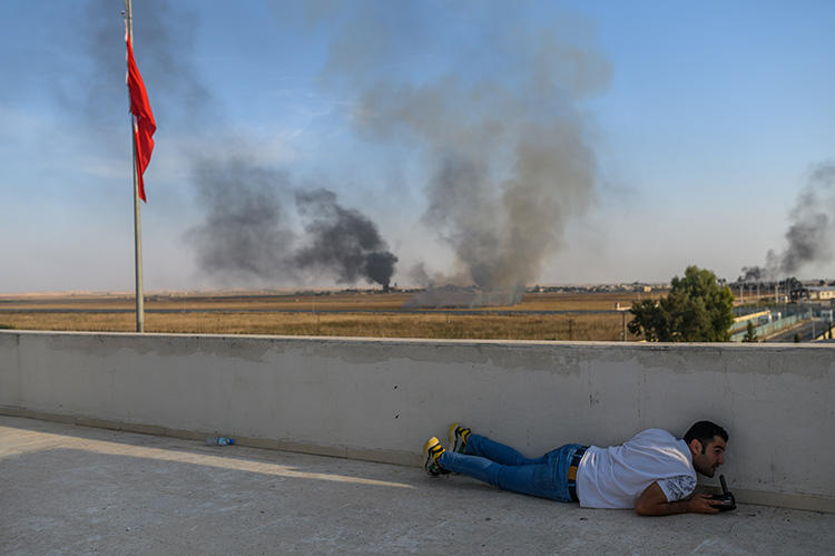 A journalist takes cover in Akcakale near the Turkish border with Syria on October 10, 2019, as a mortar landed nearby, on the second day of Turkey's military operation against Kurdish forces in Syria. At least seven journalists were killed in Syria in 2019, including three in Turkish airstrikes in October. (AFP/Bulent Kilic)