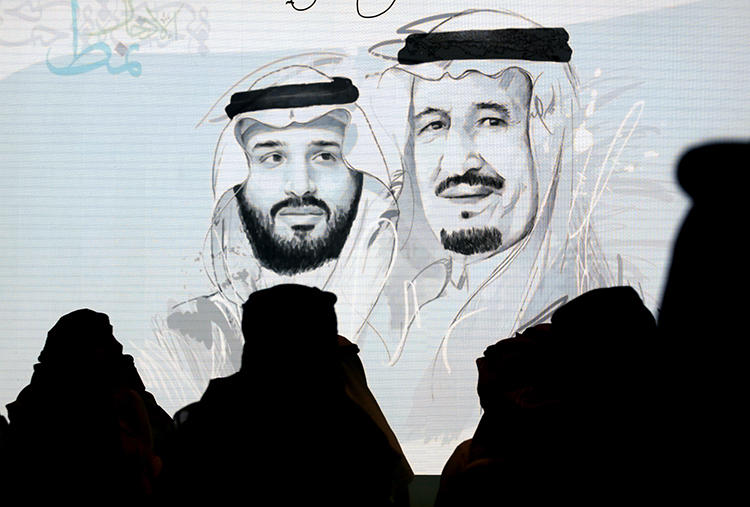 Saudi participants at the Future Investment Initiative stand for the national anthem in front of a screen displaying images of Saudi King Salman, right, and Crown Prince Mohammed bin Salman, on October 28, 2019, in Riyadh. Saudi Arabia had at least 26 journalists in prison at the end of 2019. (AP Photo/Amr Nabil)