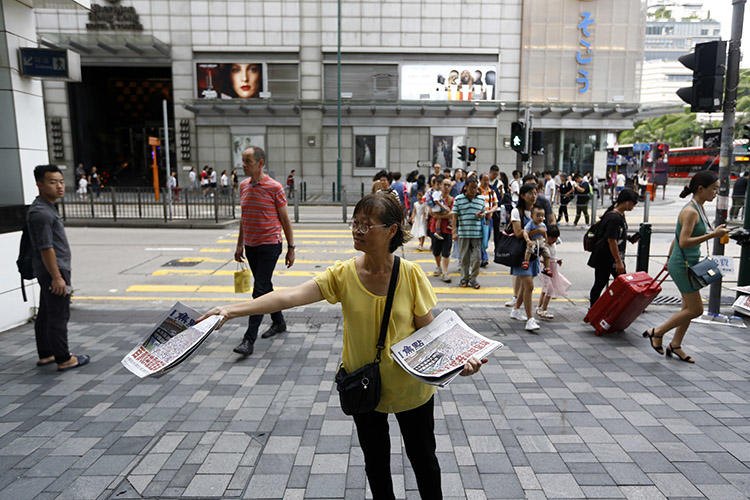 2019年7月7日，香港一名女士在備受大陸遊客歡迎的商業區分發報紙，其頭版新聞標題為《百萬人抗共震驚全球》。（美聯社/ Andy Wong）