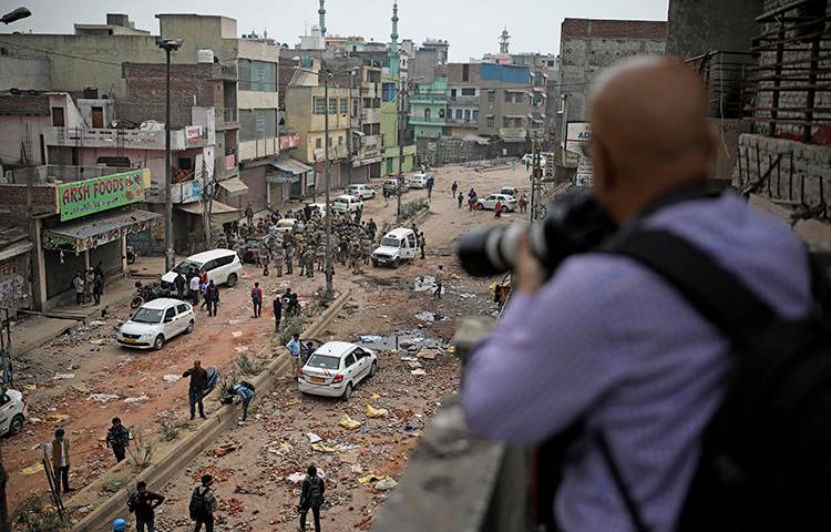 A journalist photographs soldiers patrolling a street following riots in New Delhi, India, on February 27, 2020. At least a dozen journalists were attacked or harassed covering the riots. (AP/Altaf Qadri)