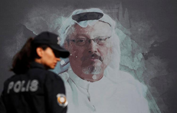 A police officer is seen near a picture of slain Saudi journalist Jamal Khashoggi in Istanbul, Turkey, on October 2, 2019. Today, Turkey indicted 20 Saudi nationals in Khashoggi's killing. (AP/Lefteris Pitarakis)