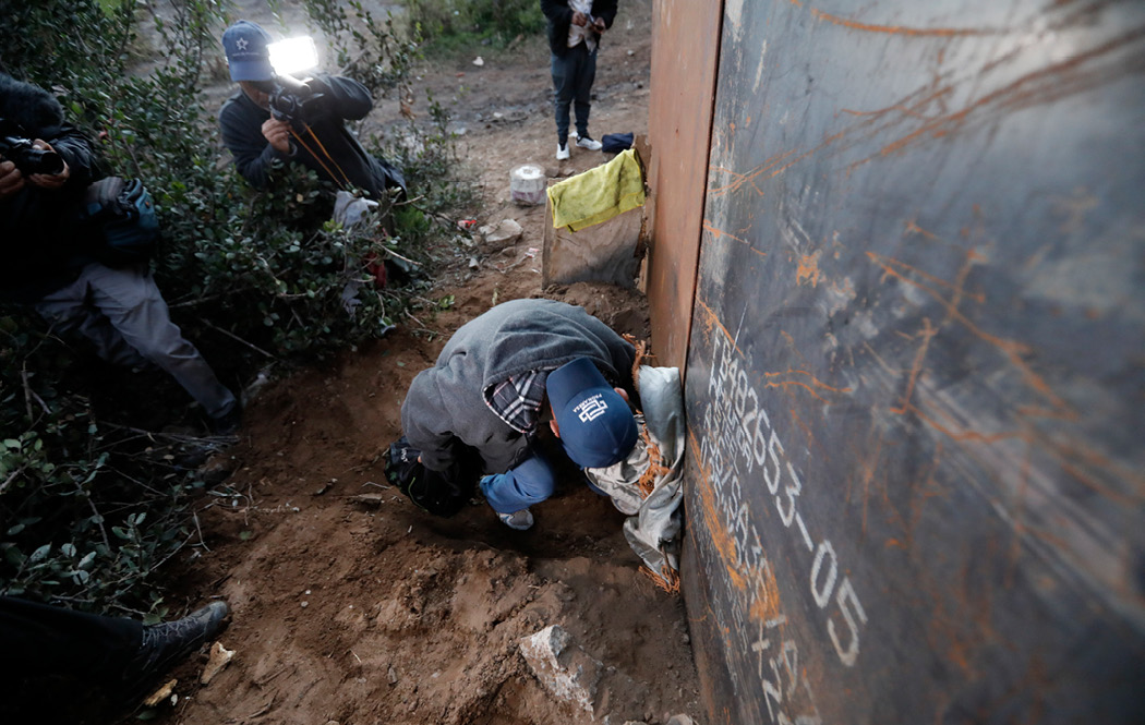 A Honduran migrant crawls through a hole under the U.S. border fence as journalists take pictures, in Playas de Tijuana, Mexico, on December 4, 2018. U.S. Customs and Border Protection monitored some journalists covering migration in a secret database. (AP/Rebecca Blackwell)