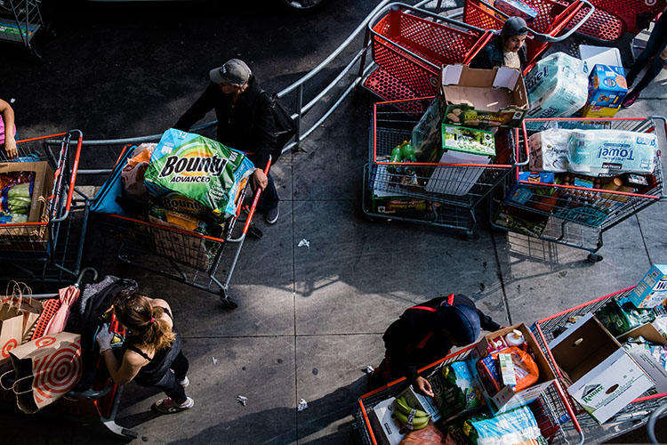 People wait for their rides with carts full of groceries preparing for social distancing at East River Plaza in New York City on March 13, 2020. (Gabriela Bhaskar for The New York Times)