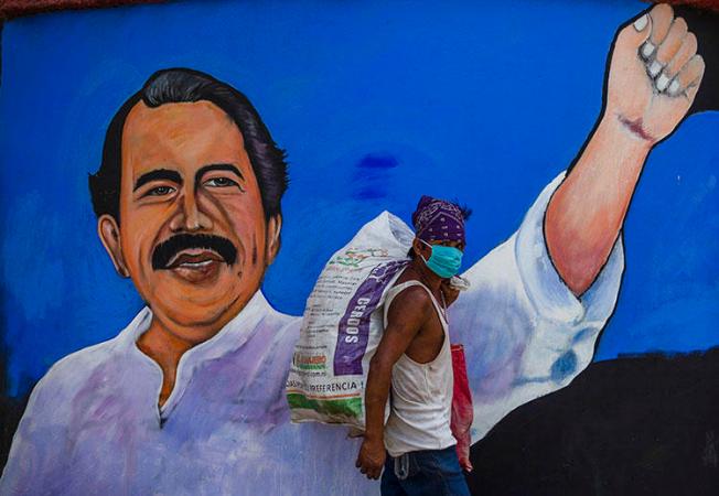 A homeless man wears a face mask against the spread of COVID-19 as he walks past a mural depicting Nicaraguan President Daniel Ortega, in Managua on April 9, 2020. Journalist Álvaro Navarro recently described to CPJ his experiences covering the pandemic in Nicaragua. (AFP/Inti Ocon)