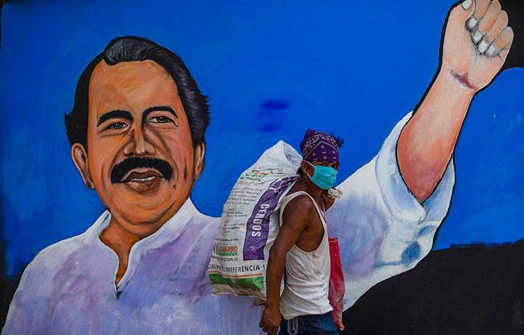 A homeless man wears a face mask against the spread of COVID-19 as he walks past a mural depicting Nicaraguan President Daniel Ortega, in Managua on April 9, 2020. Journalist Álvaro Navarro recently described to CPJ his experiences covering the pandemic in Nicaragua. (AFP/Inti Ocon)