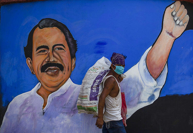 Un desamparado lleva puesta una mascarilla facial para evitar la propagación del COVID-19 mientras camina frente a un mural con la figura del presidente nicaragüense Daniel Ortega, en Managua el 9 de abril de 2020. Recientemente el periodista Álvaro Navarro relató al CPJ las experiencias que ha vivido cubriendo la pandemia en Nicaragua. (AFP/Inti Ocon)