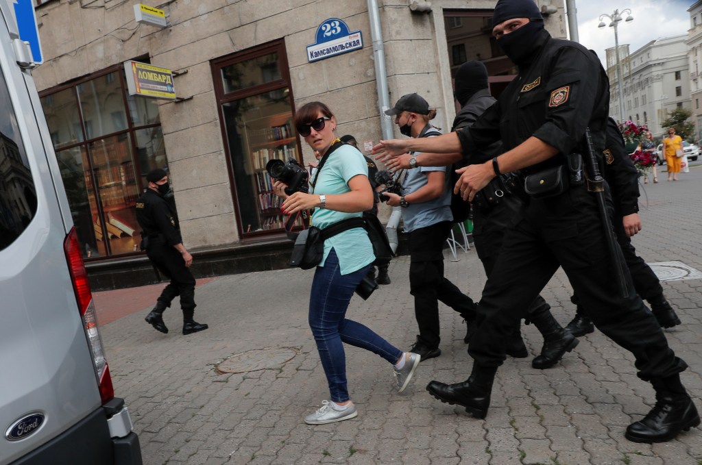 In a street scene, a police officer reaches towards a woman carrying a camera