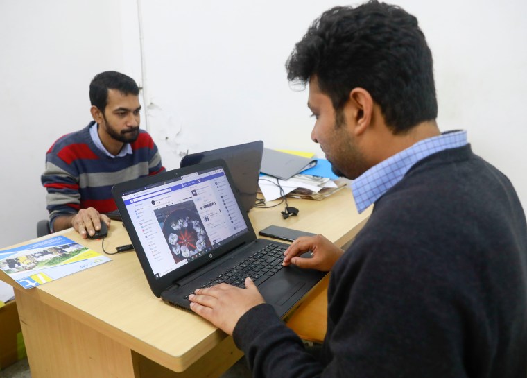 Two men use laptops on opposite sides of a desk