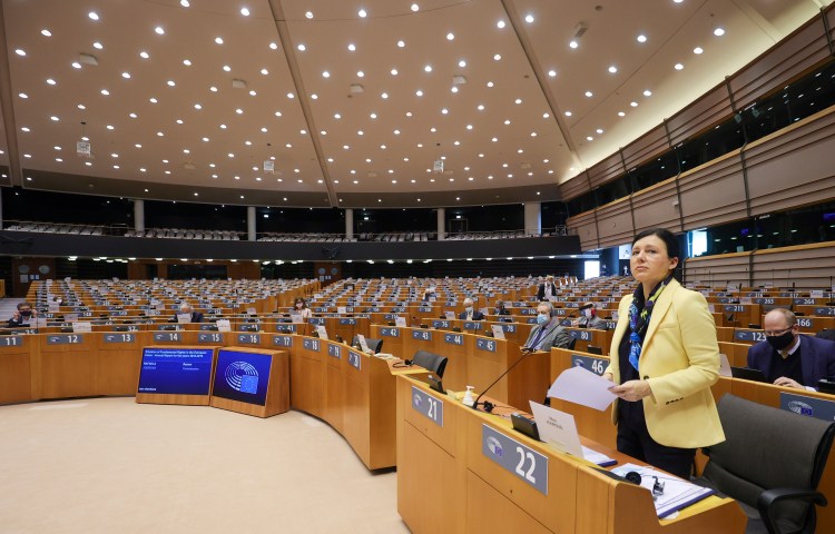 A woman in a yellow jacket stands at a row of work benches in the European Parliament.