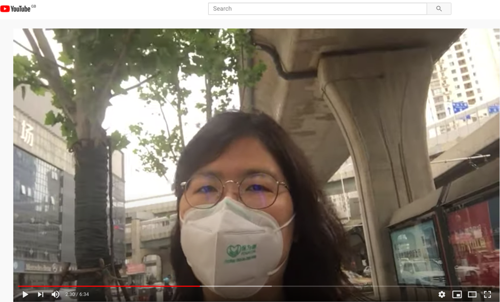 A woman in a face mask is seen addressing the camera in a YouTube vide.