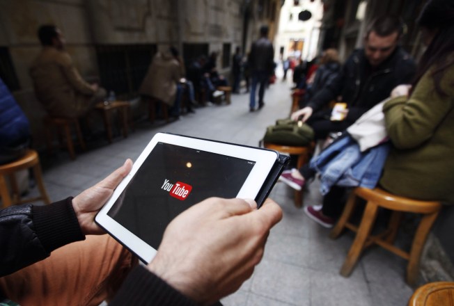 A man's hands hold a tablet against a backdrop of people seated in groups.