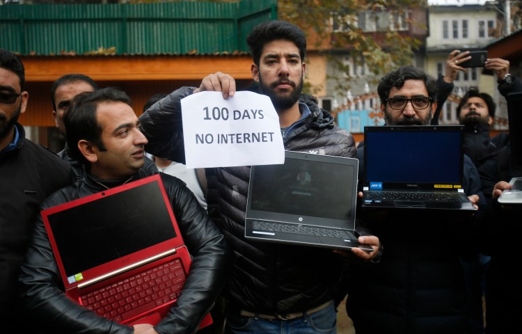 A group of men are pictured holding powered off laptops and a placard reading "100 days no internet."