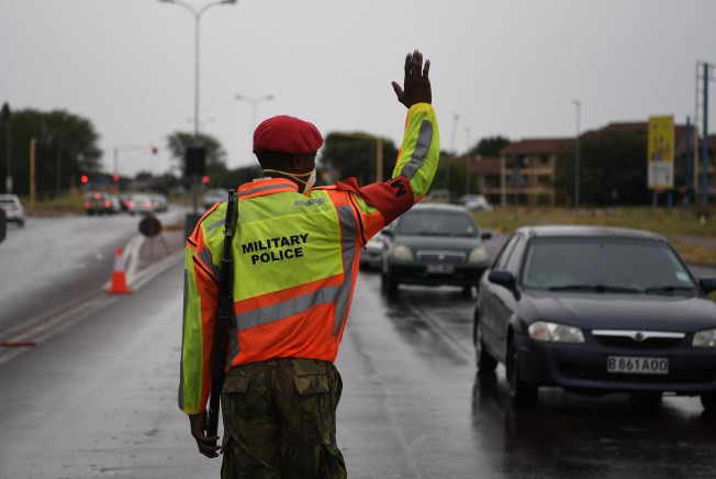 An armed officer on a street raises his hand to stop cars.