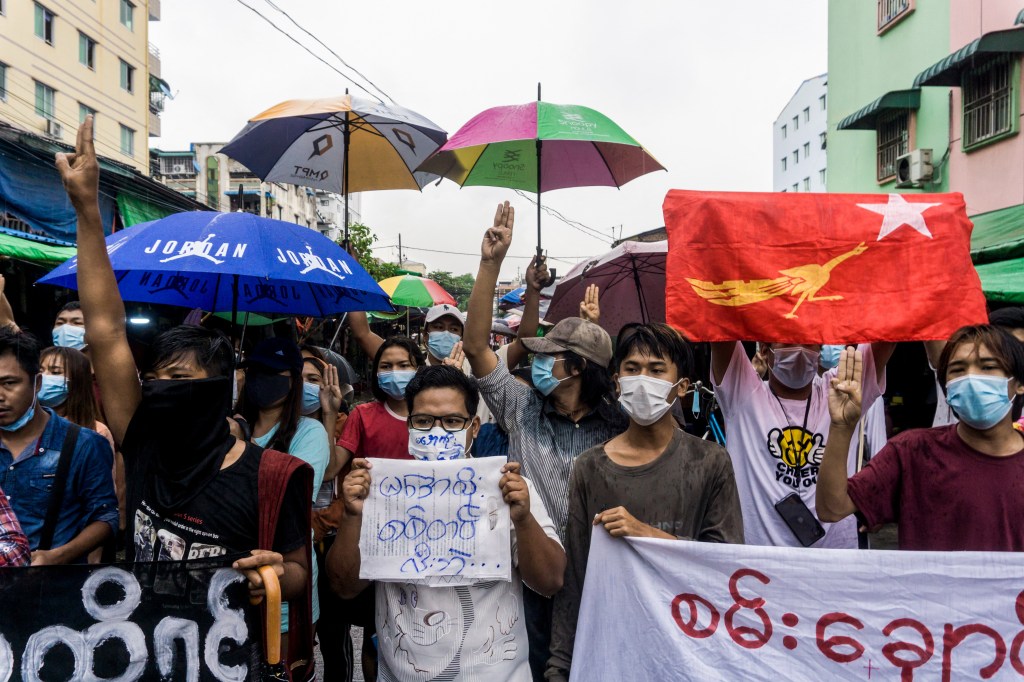 A group of people holding protest signs and umbrellas gather in a city street.