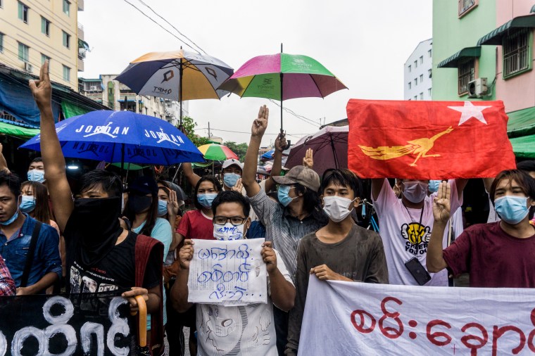 A group of people holding protest signs and umbrellas gather in a city street.