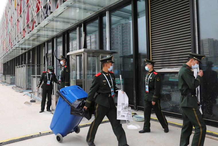 Men in uniforms and masks stand outside a large modern building..