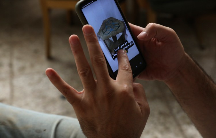 Two hands hold a phone depicting a branded table for sale and text.